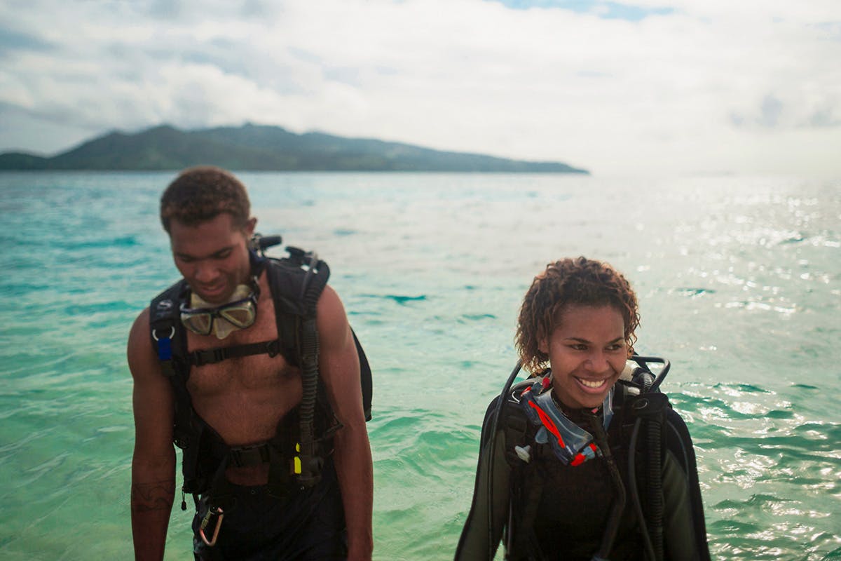 Happy woman comes out of the ocean with scuba diving gear.